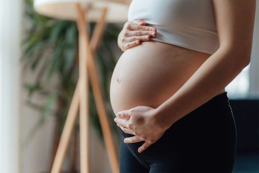 A pregnant woman is holding her belly in a living room.