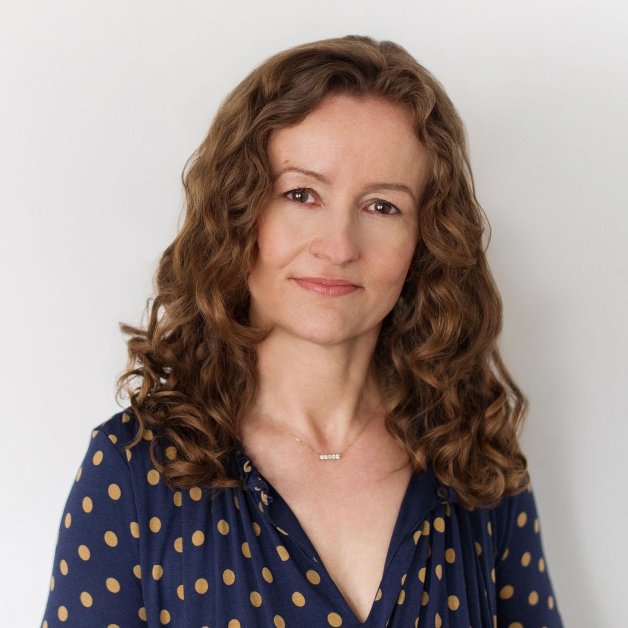 A woman with curly hair is wearing a blue polka dot shirt