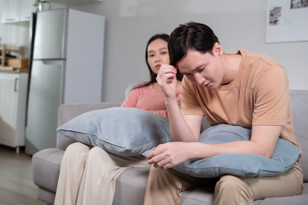 A woman is taking off her wedding ring while sitting on a couch.