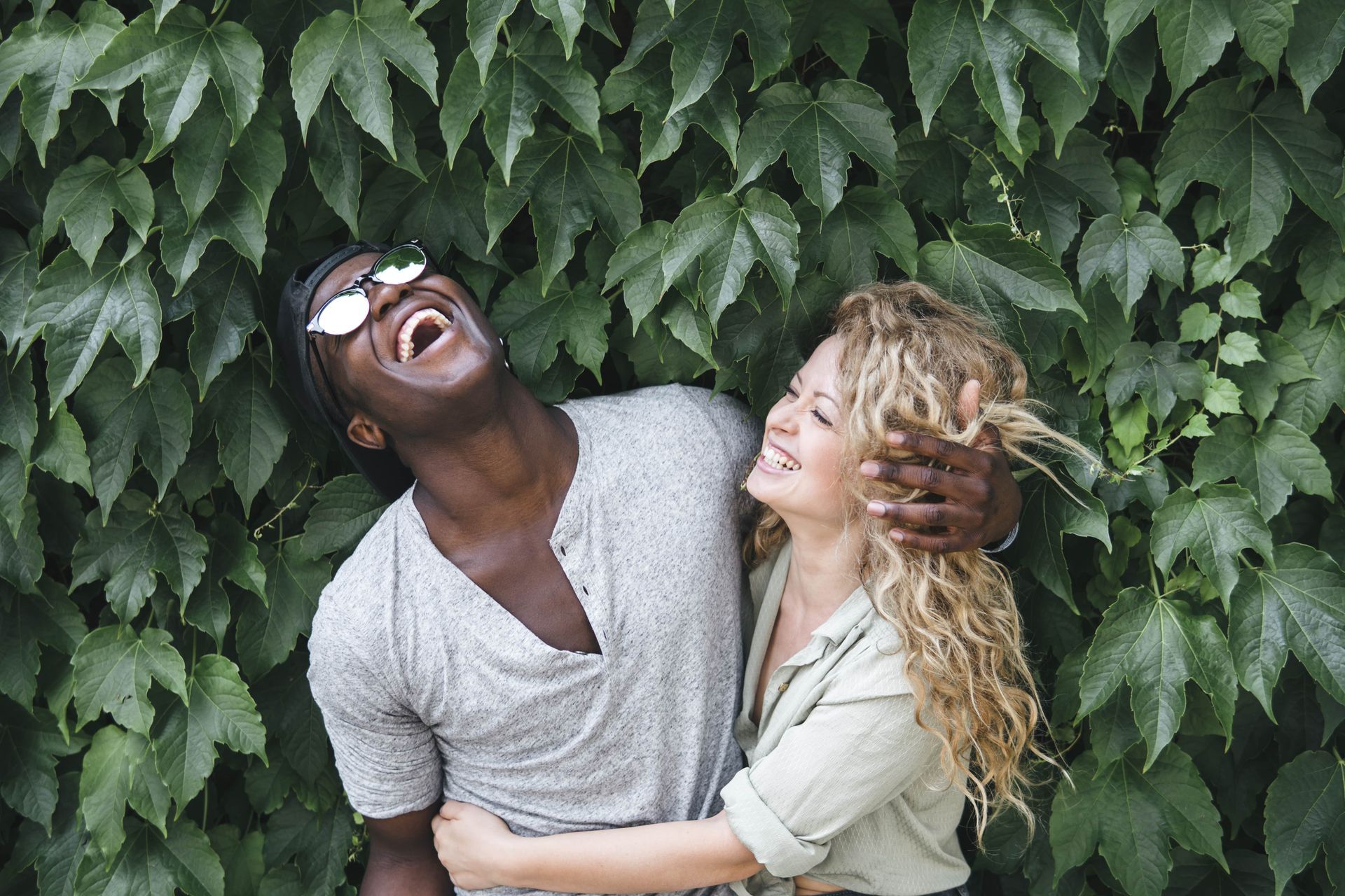 A man and a woman are laughing in front of a bush.