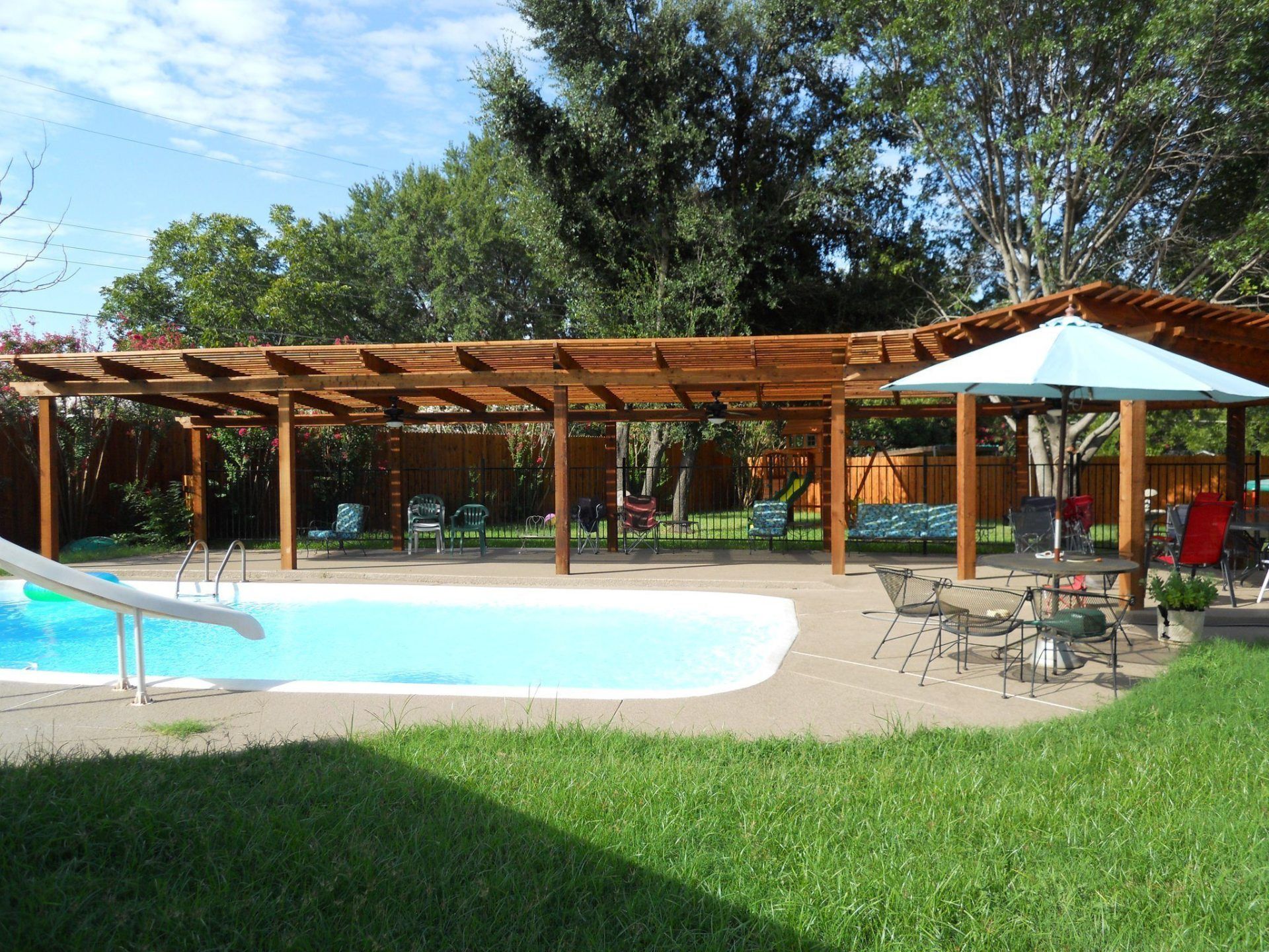 A large swimming pool with a slide under a pergola
