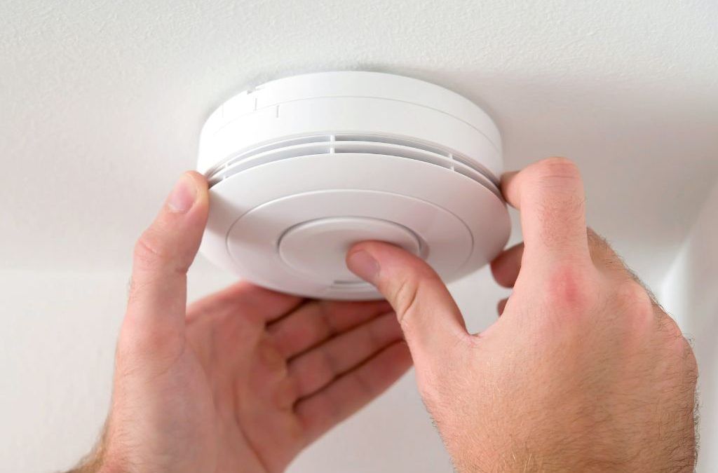 Hand pressing test button on photoelectric smoke alarm to ensure functionality and compliance in Brisbane home