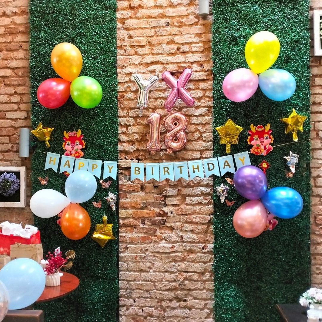 A brick wall with balloons and a banner that says happy birthday