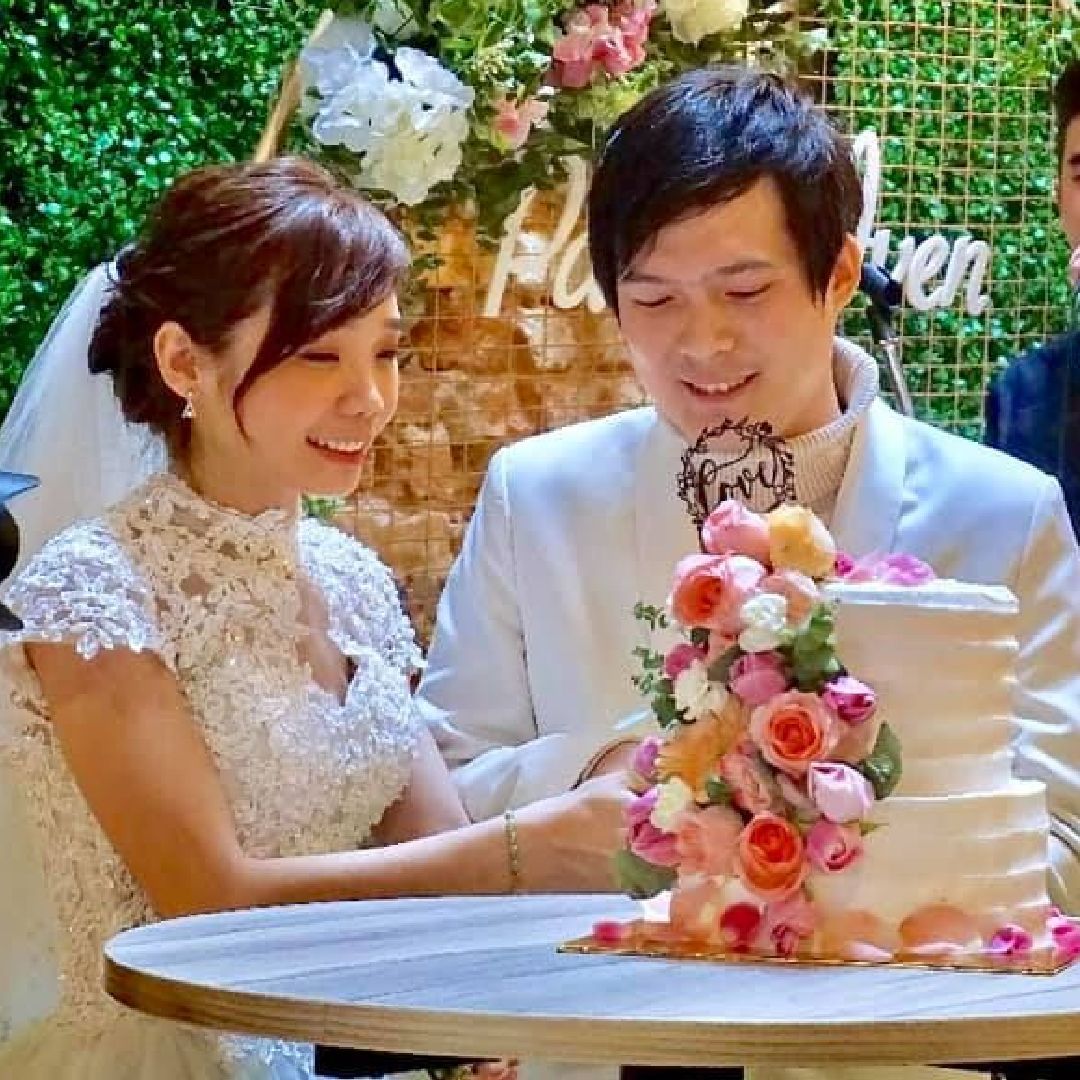 A bride and groom are sitting at a table in front of a wedding cake.