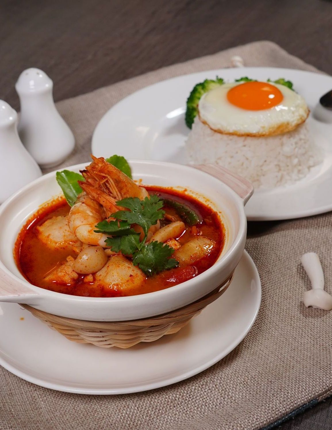 A bowl of soup next to a plate of rice with an egg on top.