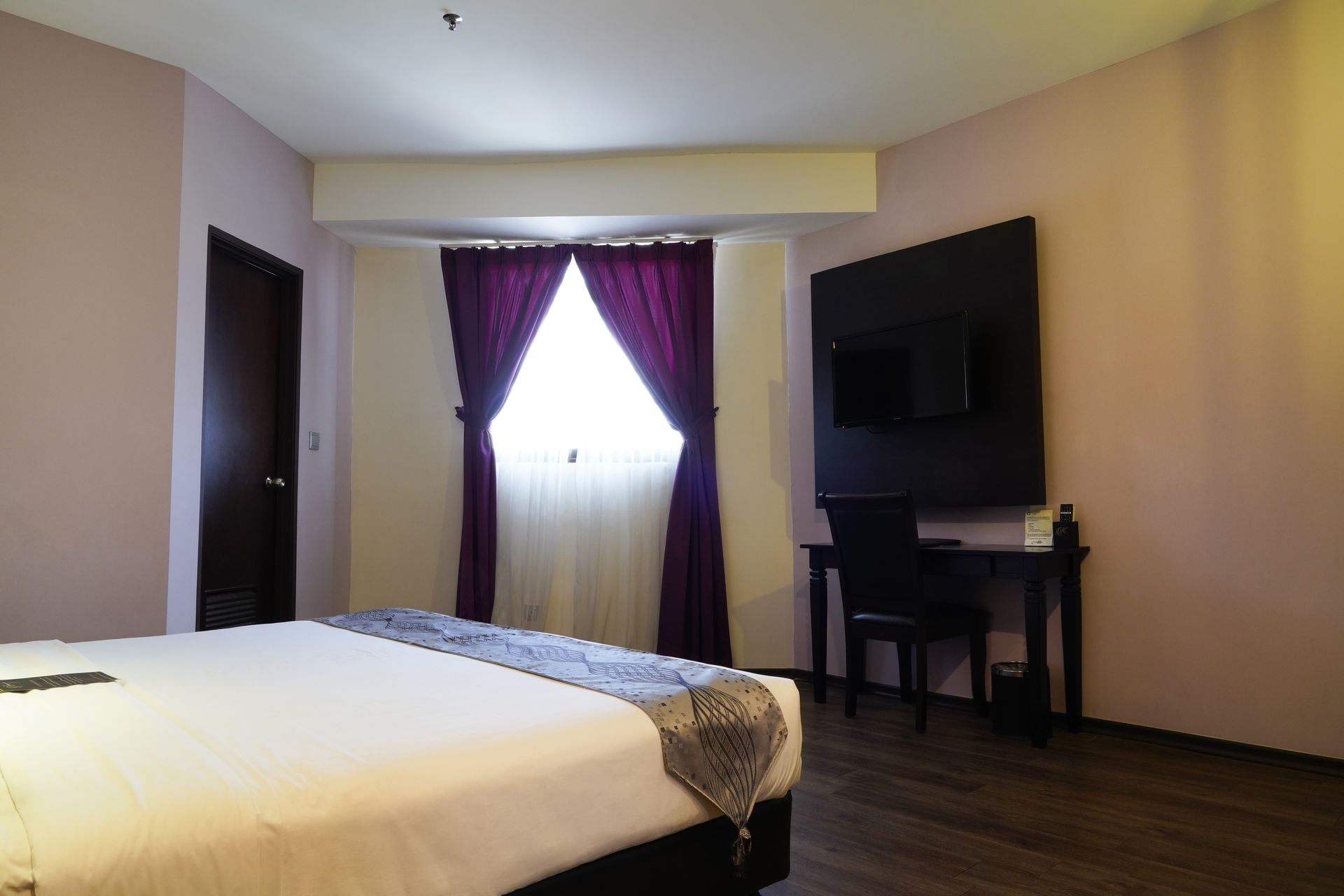A hotel room with a large bed and purple curtains