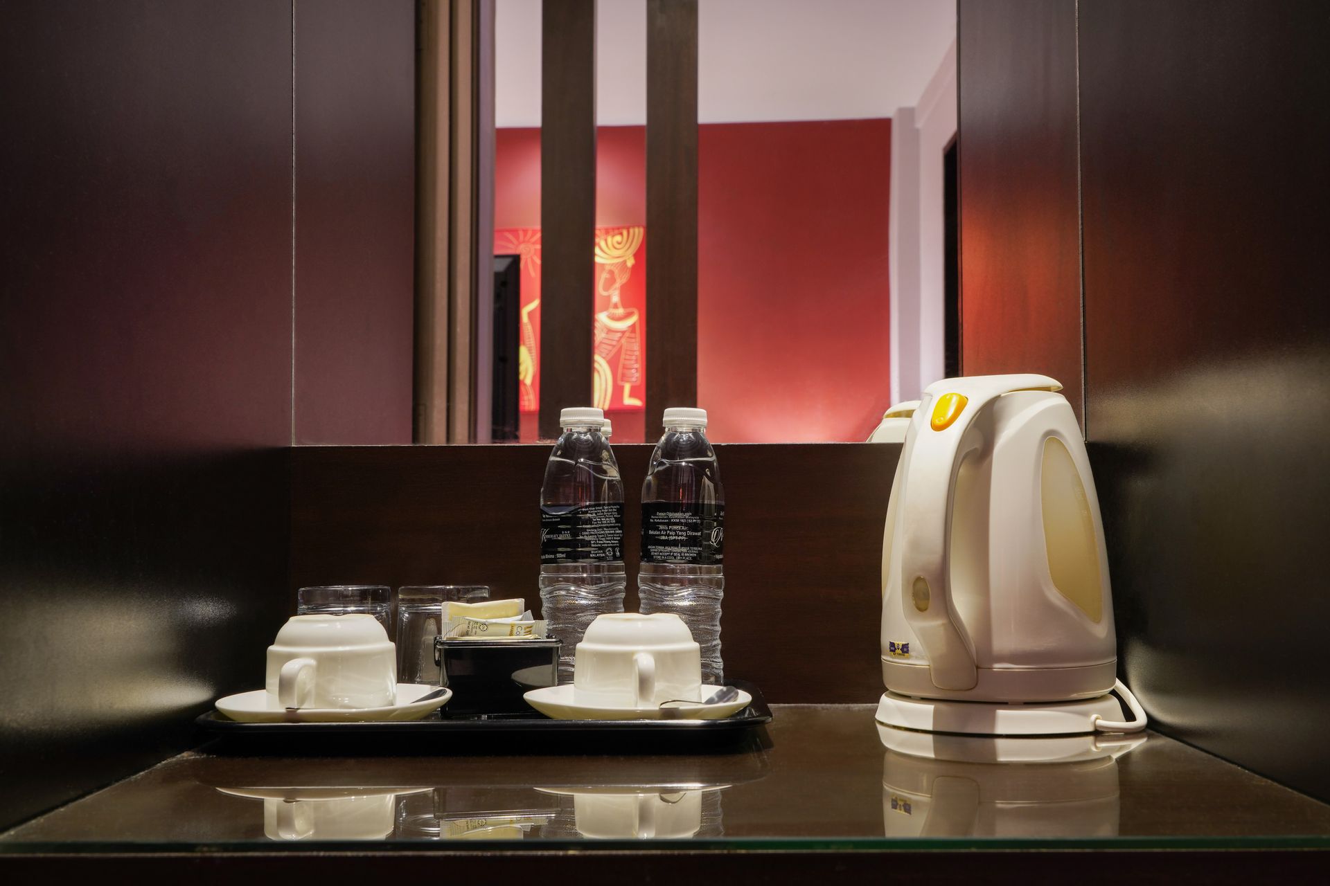 A hotel room with a kettle , cups , glasses and water bottles.