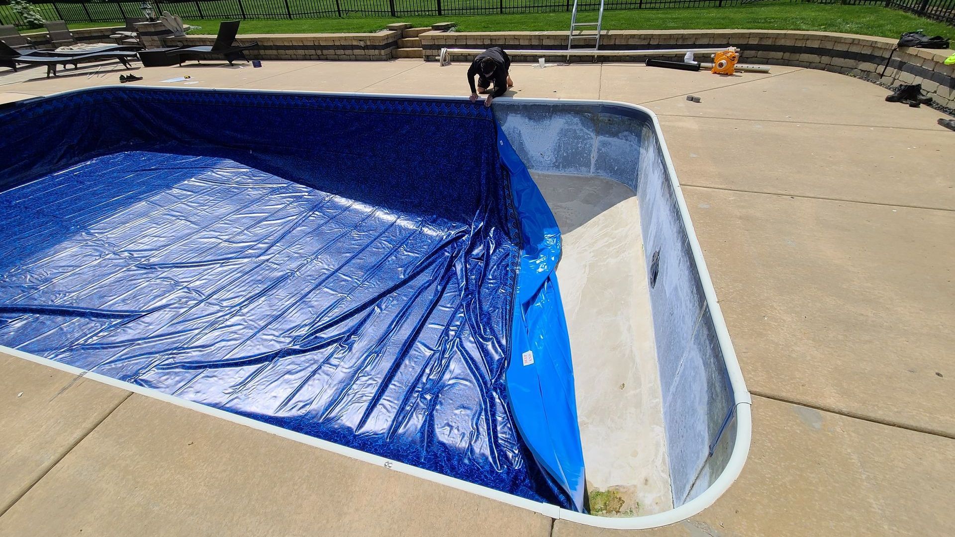 A man is covering a swimming pool with a blue tarp.