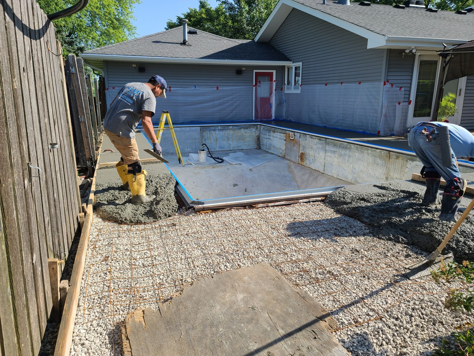 two men are working on a swimming pool in front of a house .