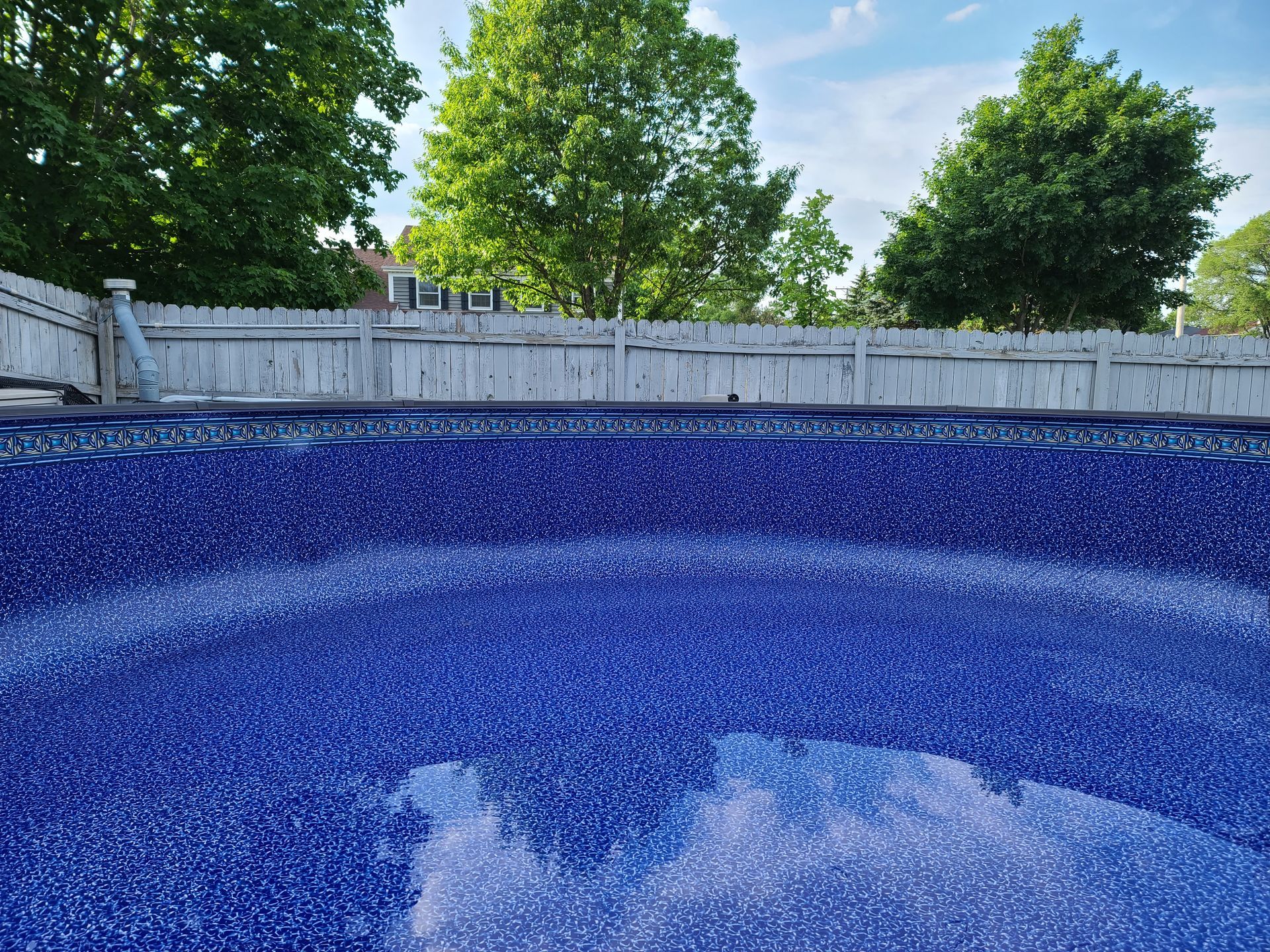 a blue swimming pool with a white fence and trees in the background .