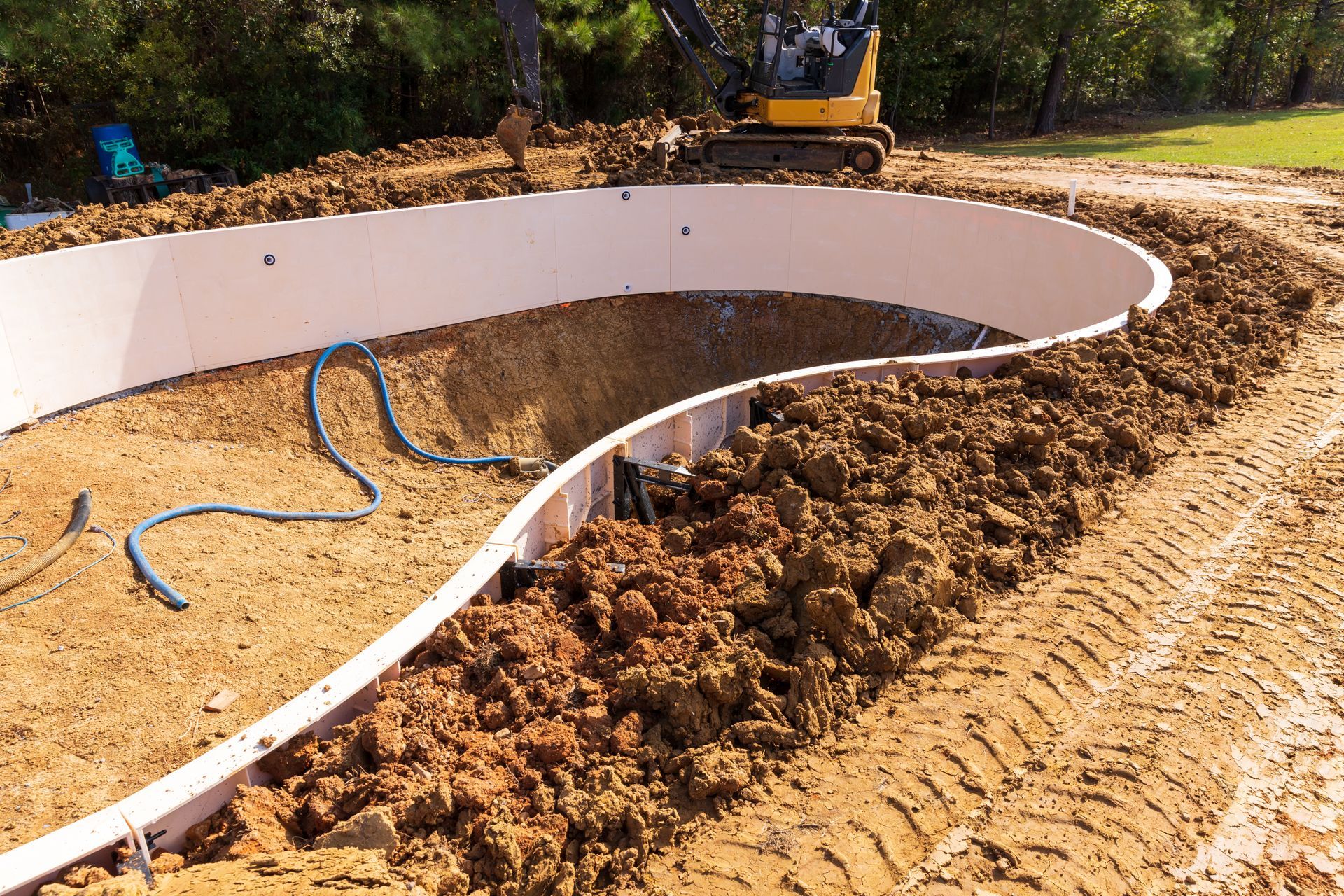 a swimming pool is being built in the dirt with a bulldozer in the background .