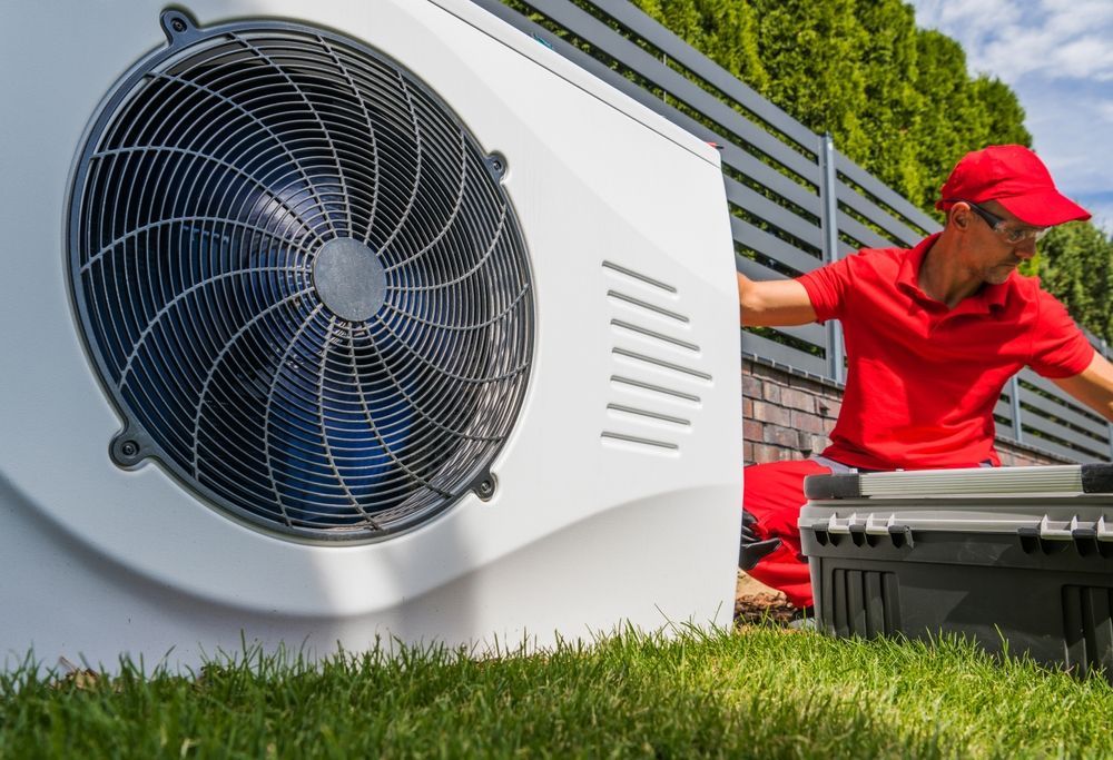 A man is sitting on the grass next to a fan.