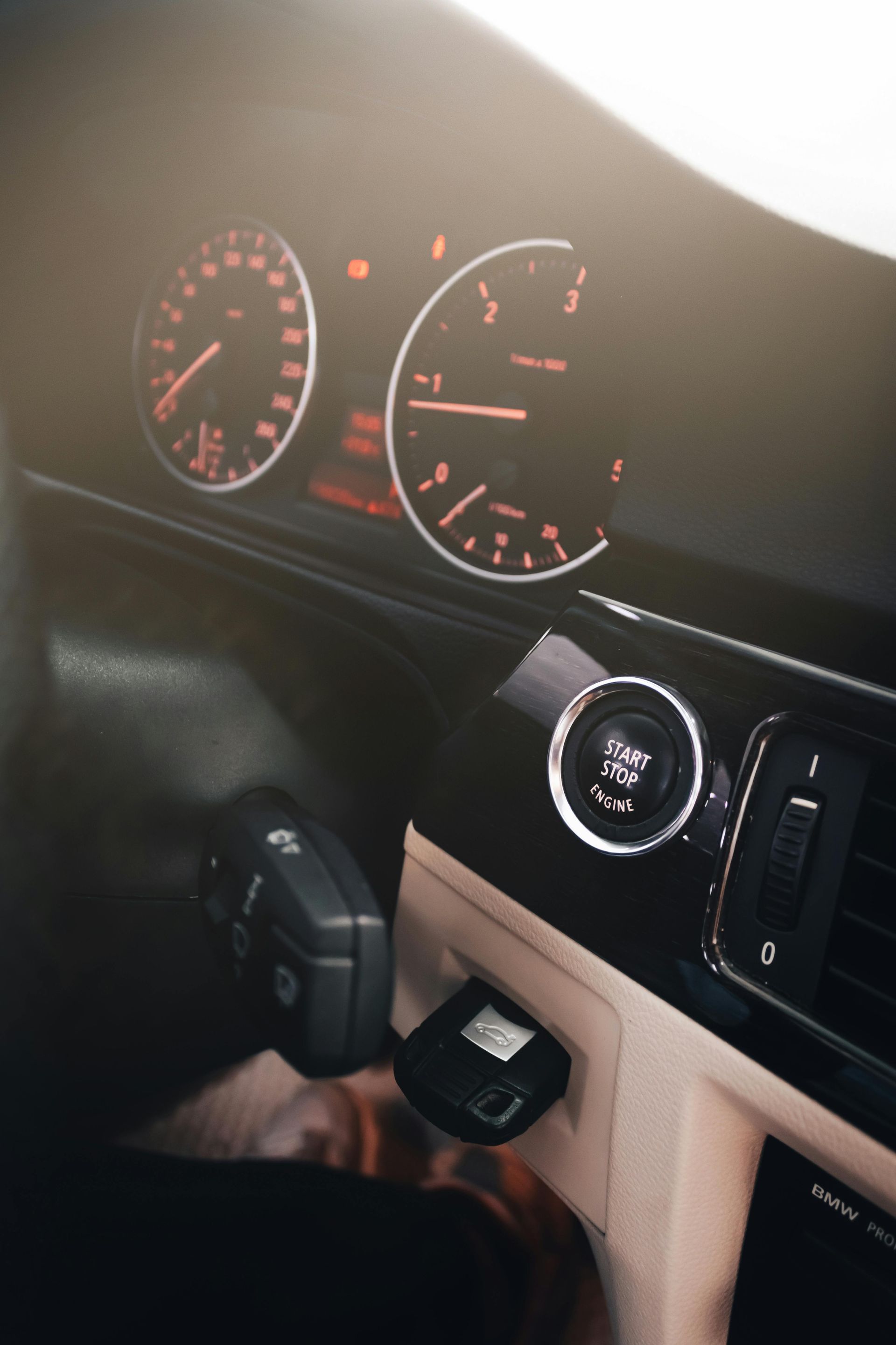 Car dashboard with gauges, ignition button, and key fob, in a warm-lit interior.