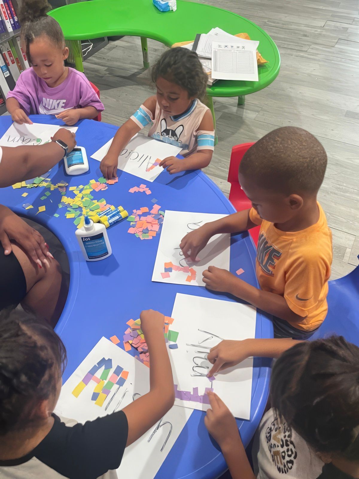 Children at a table, gluing colorful shapes onto paper.