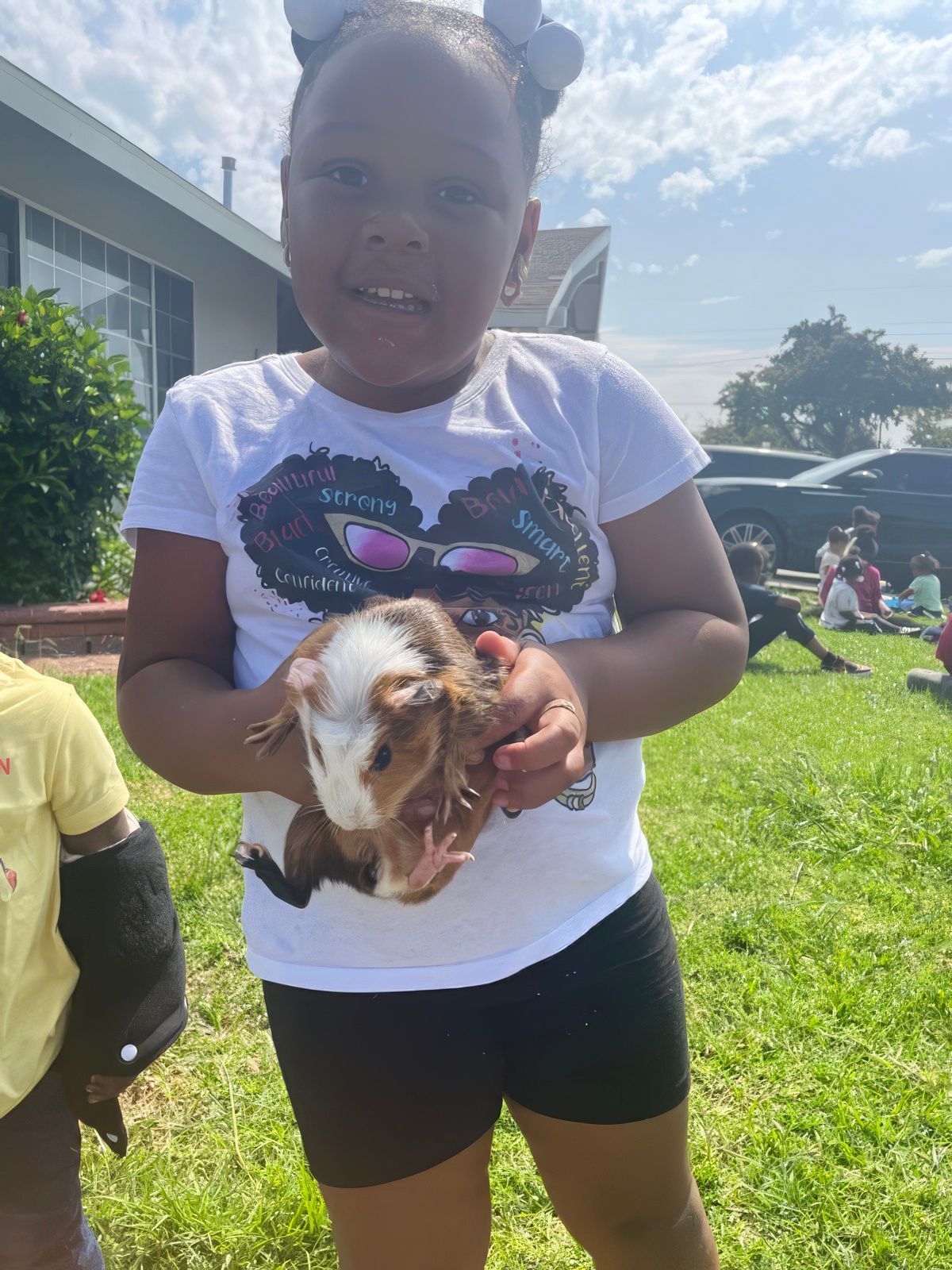 Young person holding a guinea pig in a sunny outdoor setting.