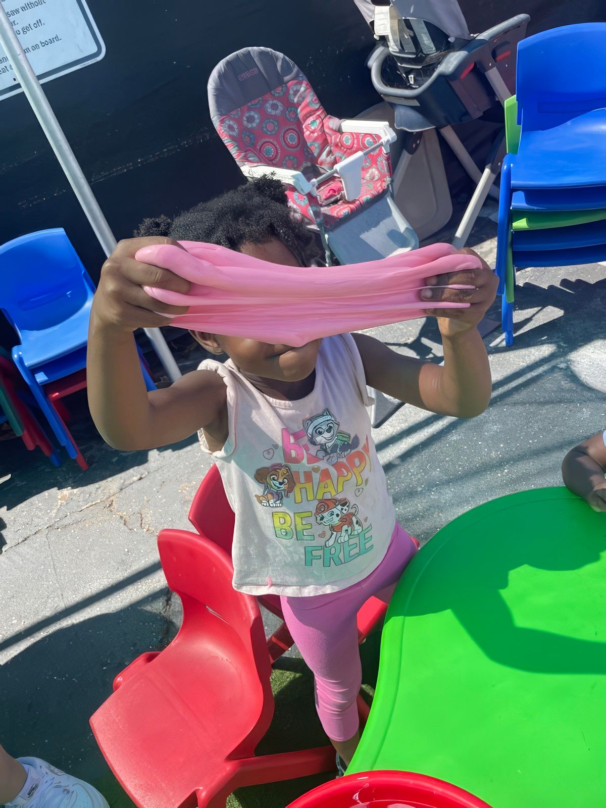 Girl playing with pink slime, outdoors. She is stretching the slime, smiling.