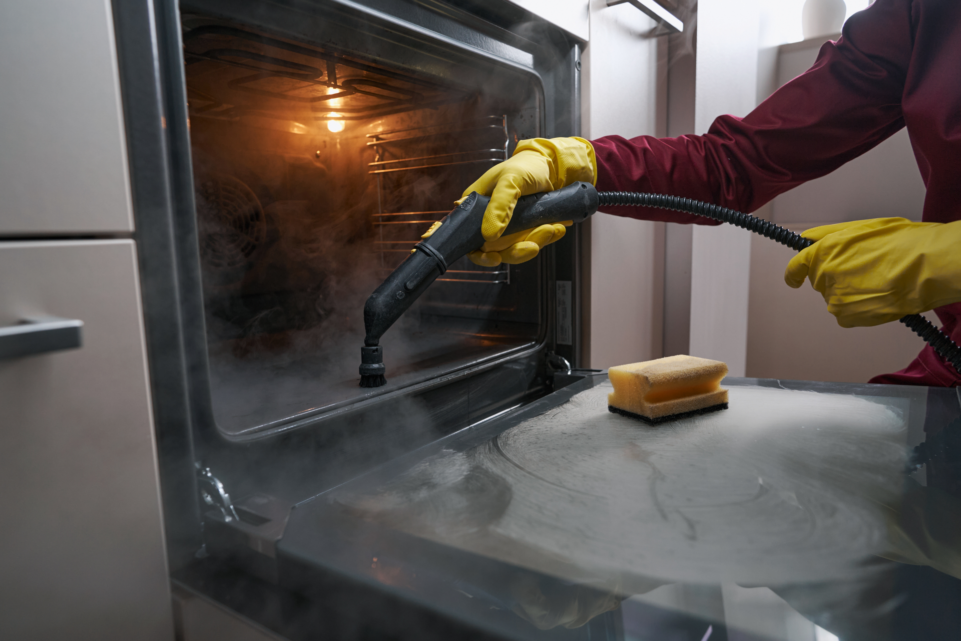 A person wearing gloves steam cleans a white bathroom sink and faucet.