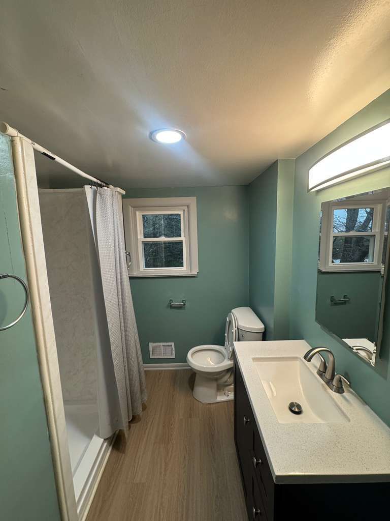 Bathroom with a toilet, sink, shower, window, and blue-green walls.