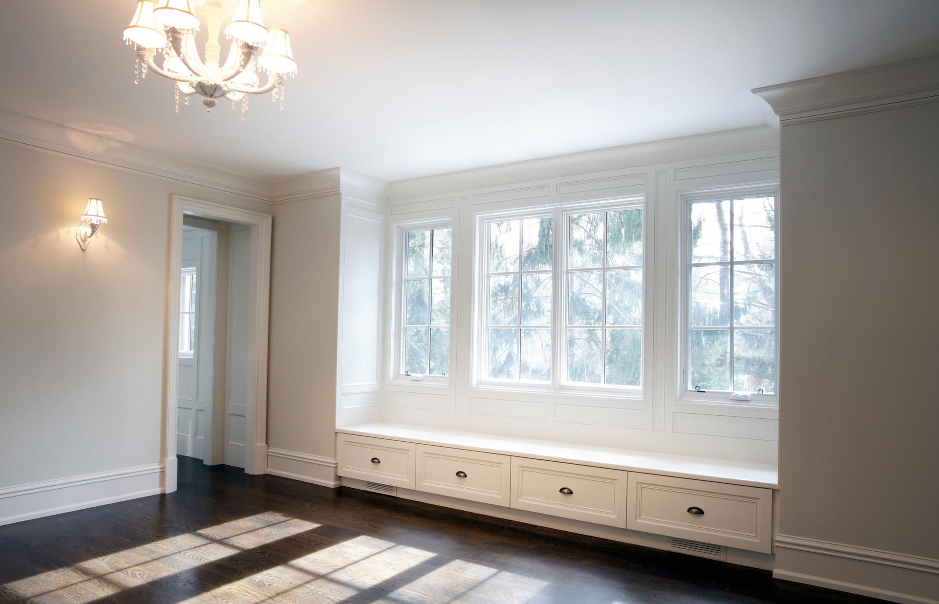 Bright room with dark floor, white trim, and a window seat with drawers under windows.