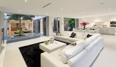 Modern white living room with open doors to a courtyard, black rug, white sofa, and a tree.