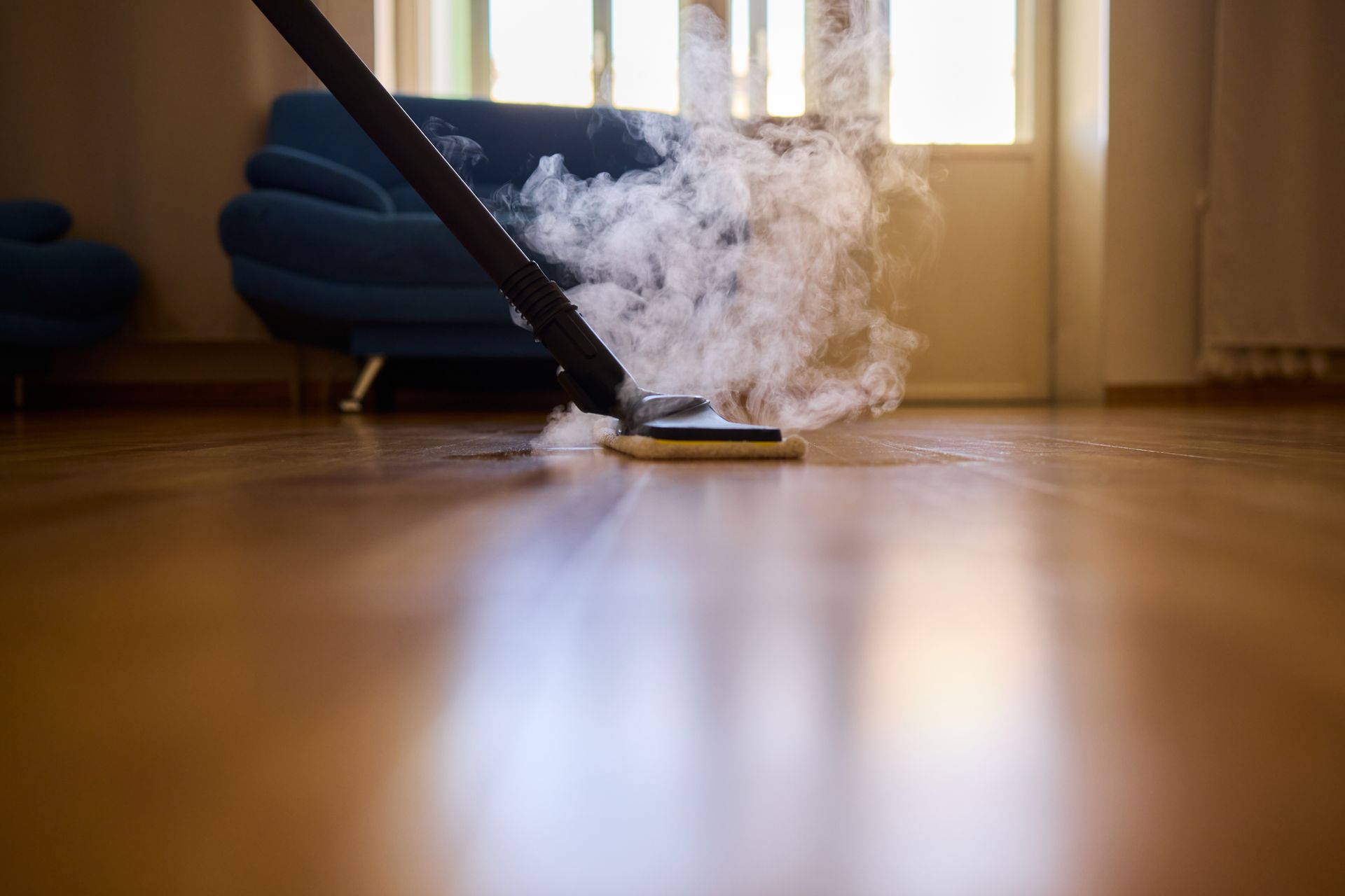 Steam cleaner cleaning hardwood floor, releasing visible steam.