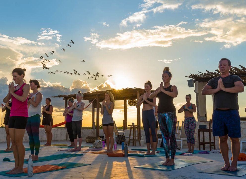 A group of people are practicing yoga on a rooftop at sunset.