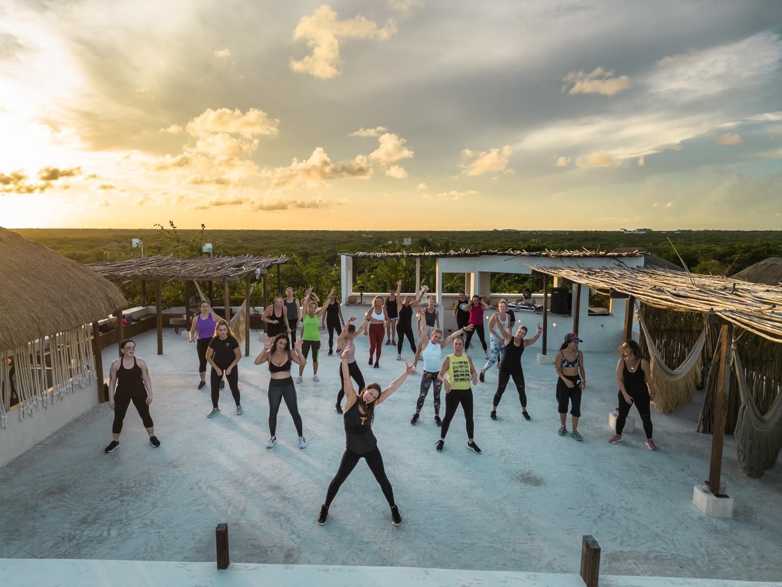 A group of people are doing exercises on a rooftop at sunset.