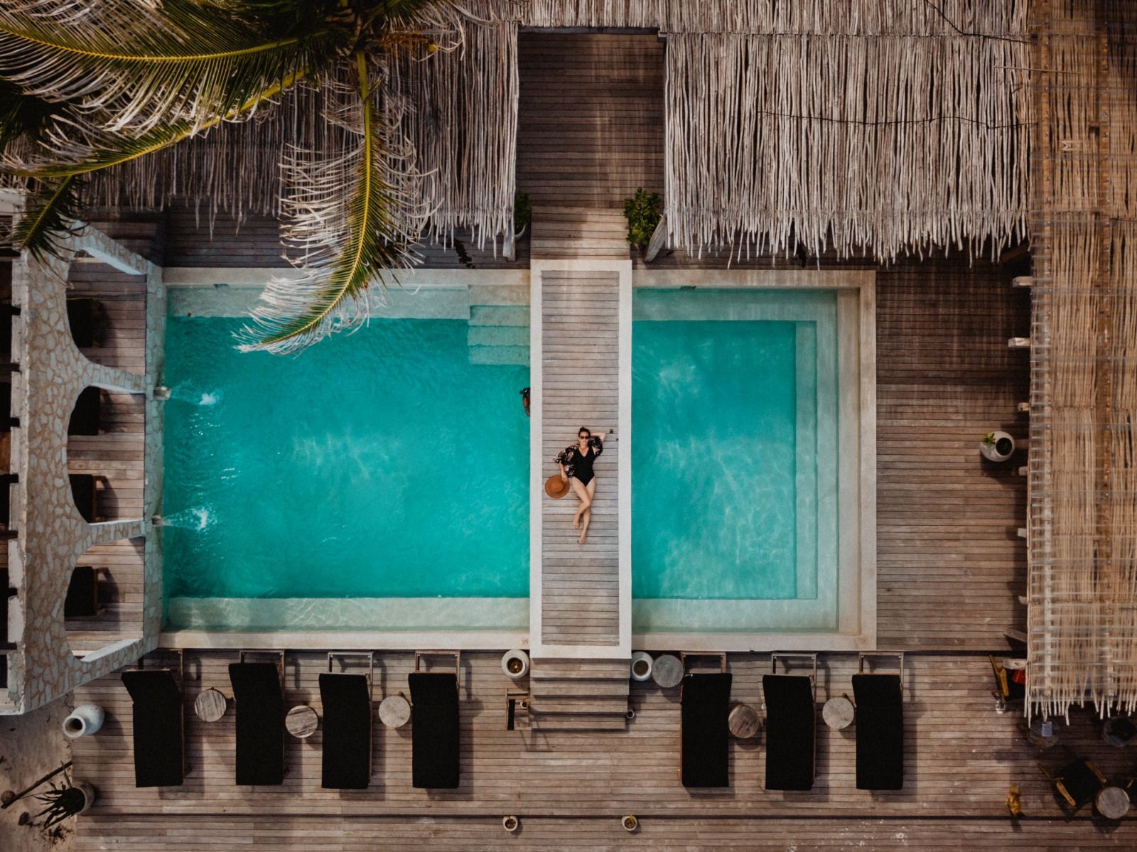 An aerial view of a woman laying on a wooden deck next to a swimming pool.