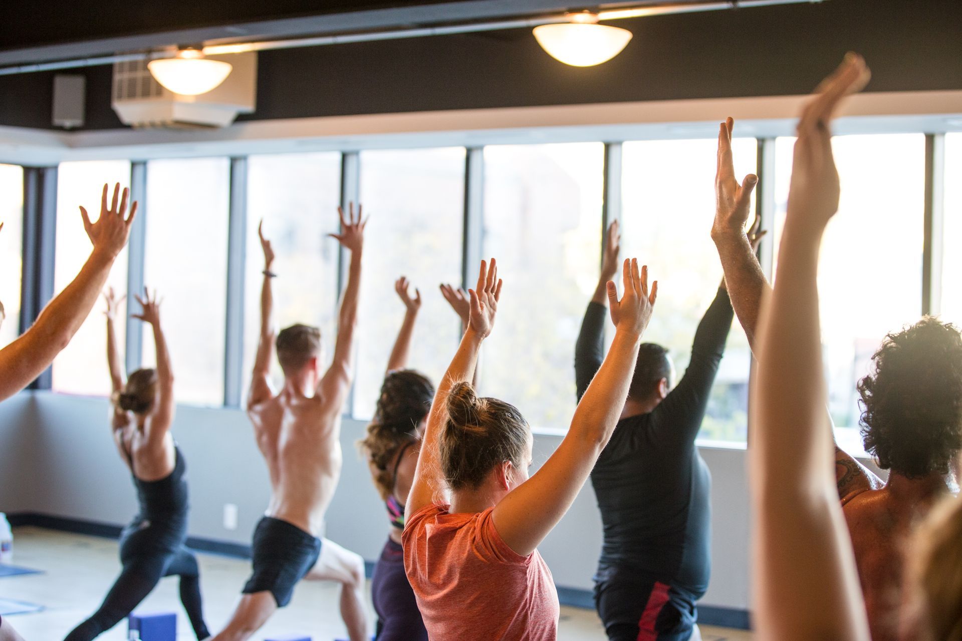 A group of people are doing yoga in a gym with their arms in the air.