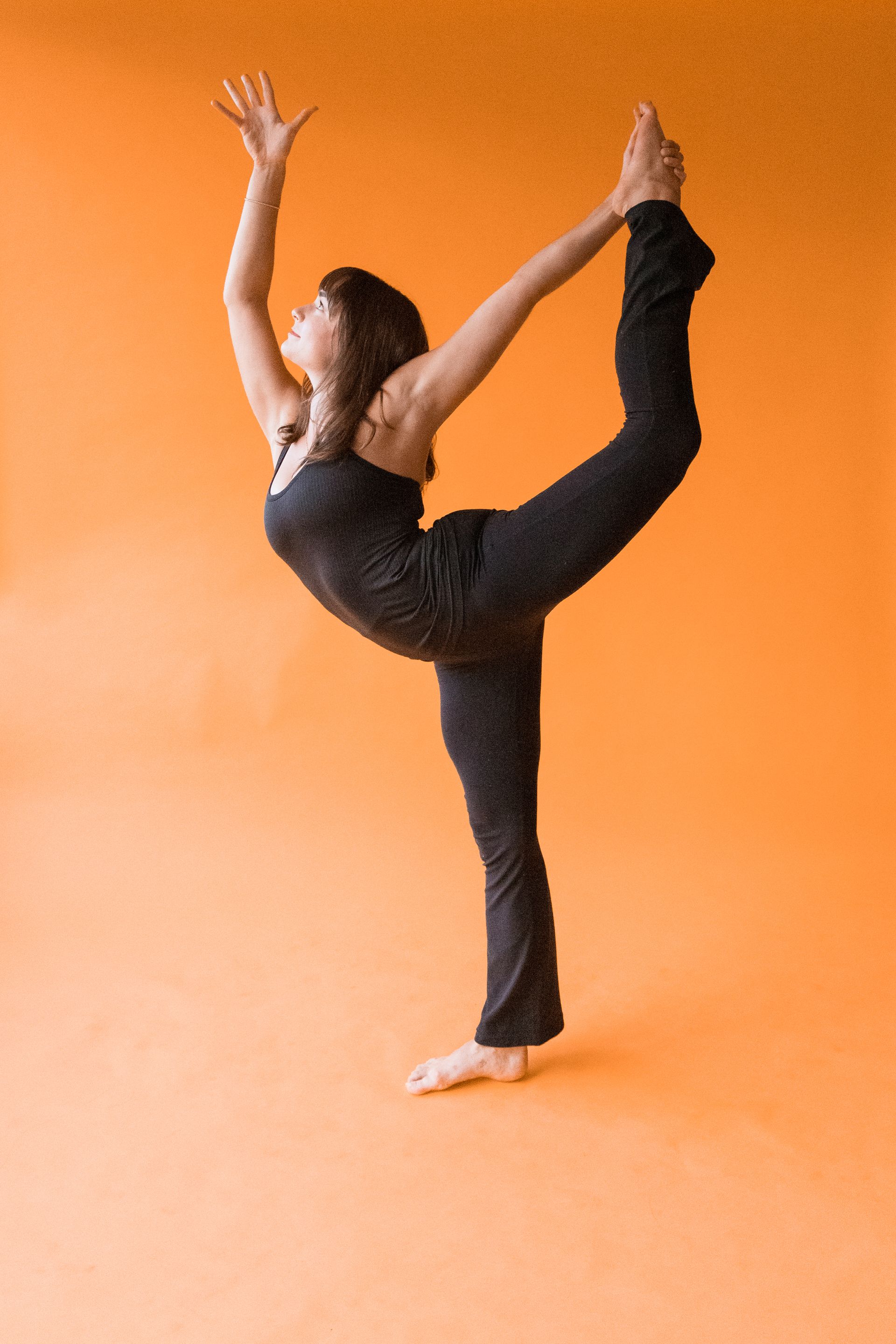 A woman is doing a yoga pose on an orange background