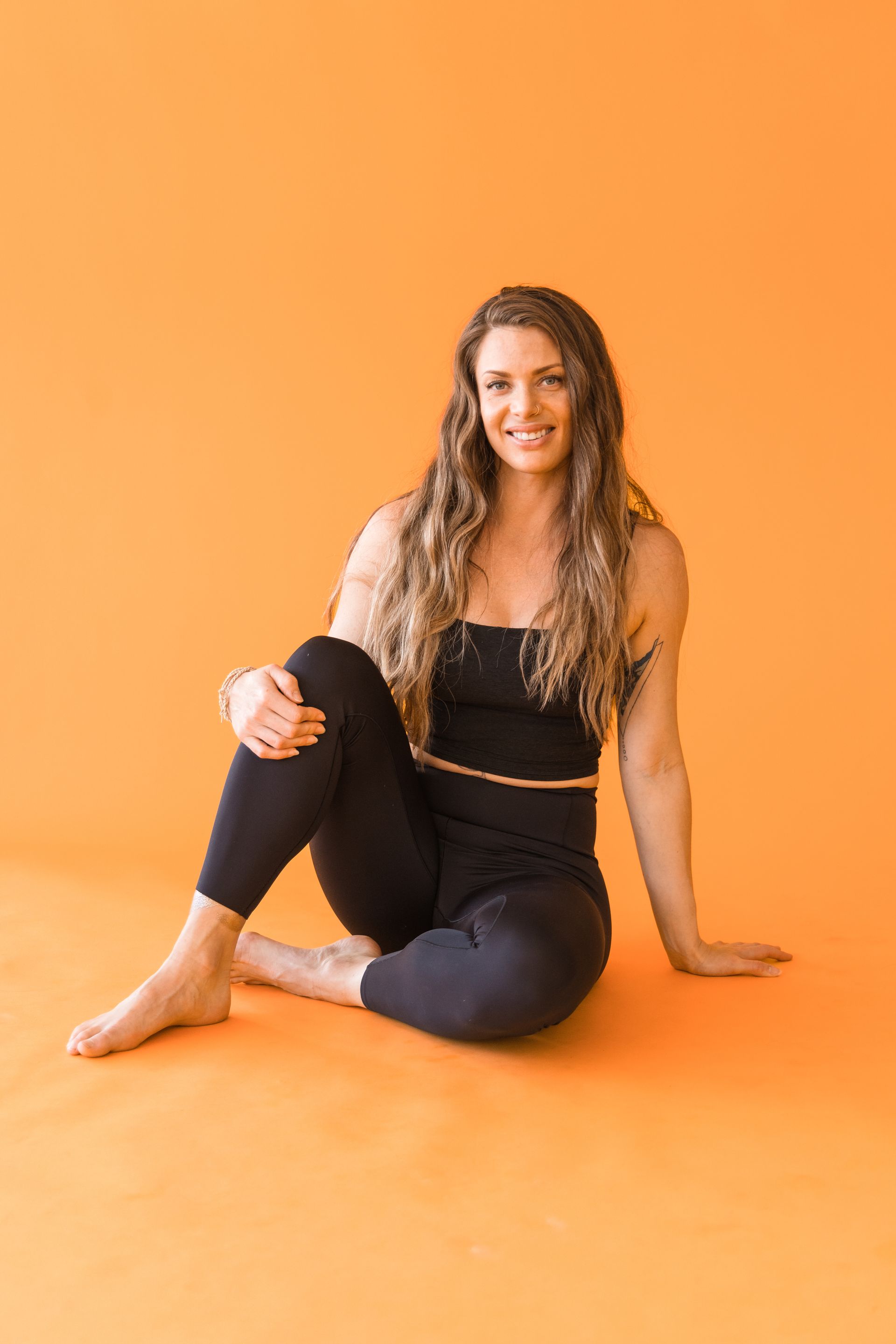 A woman is sitting on the floor with her legs crossed and smiling.