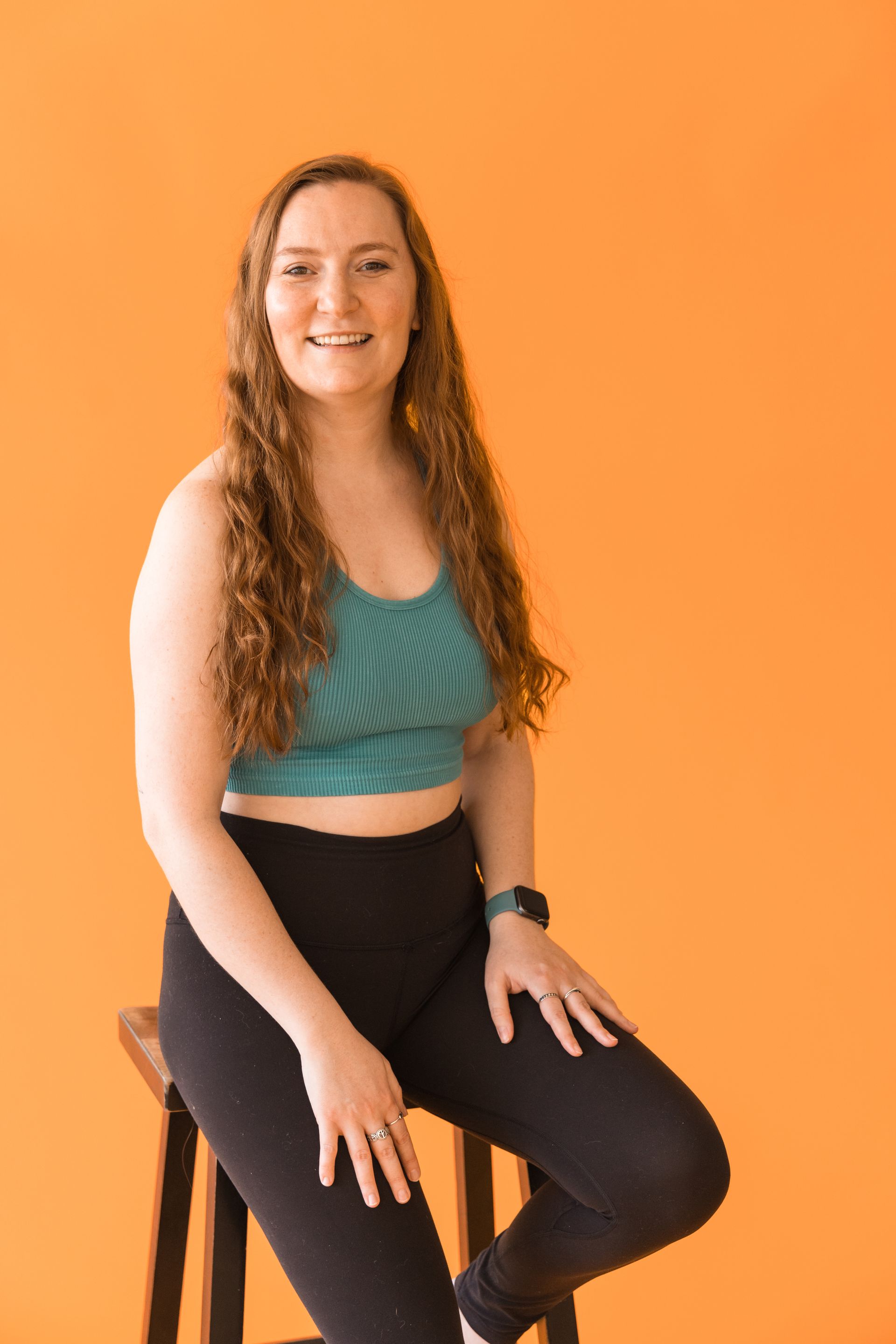 A woman is sitting on a stool in front of an orange wall.