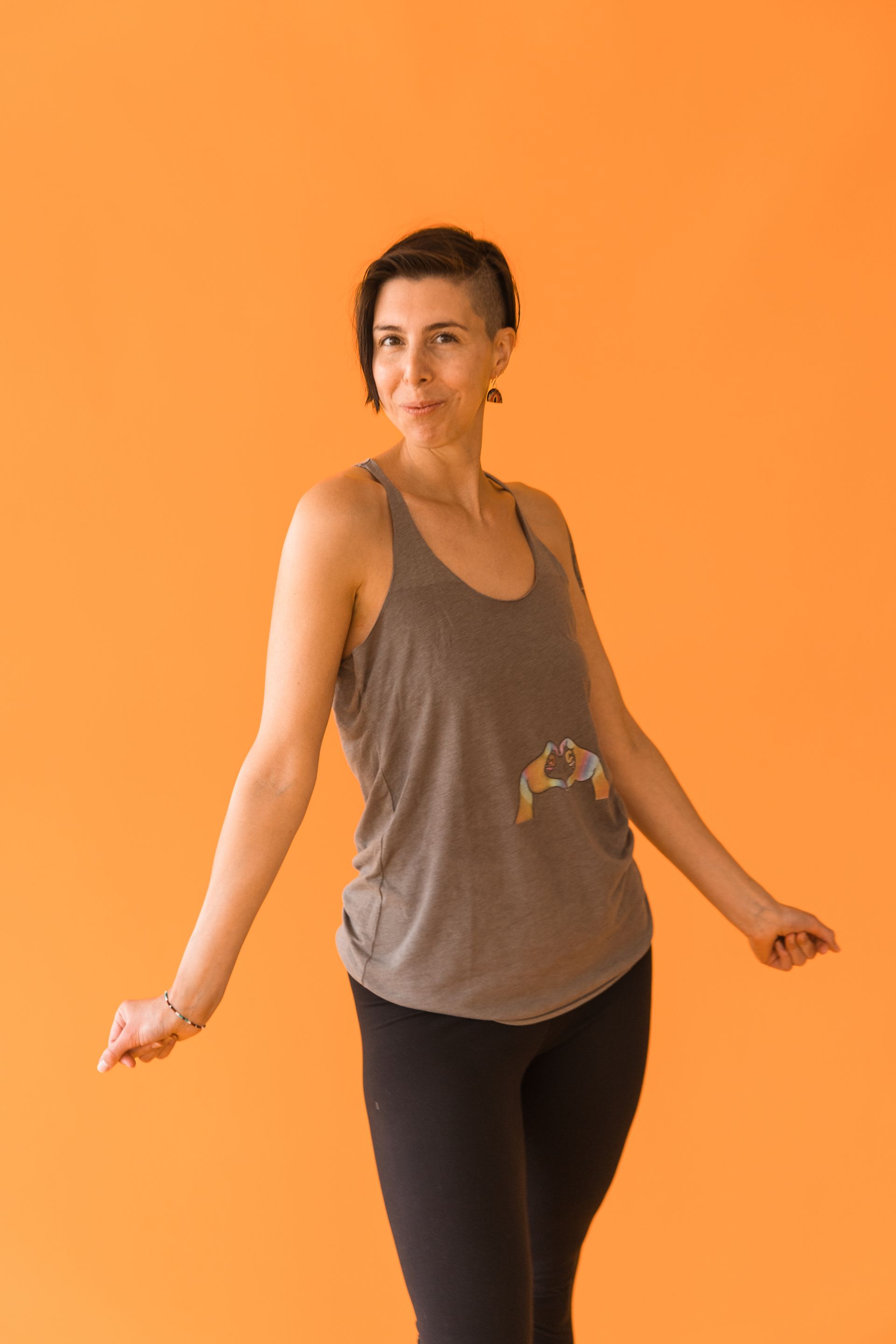 A woman in a tank top and black pants is standing in front of an orange wall.