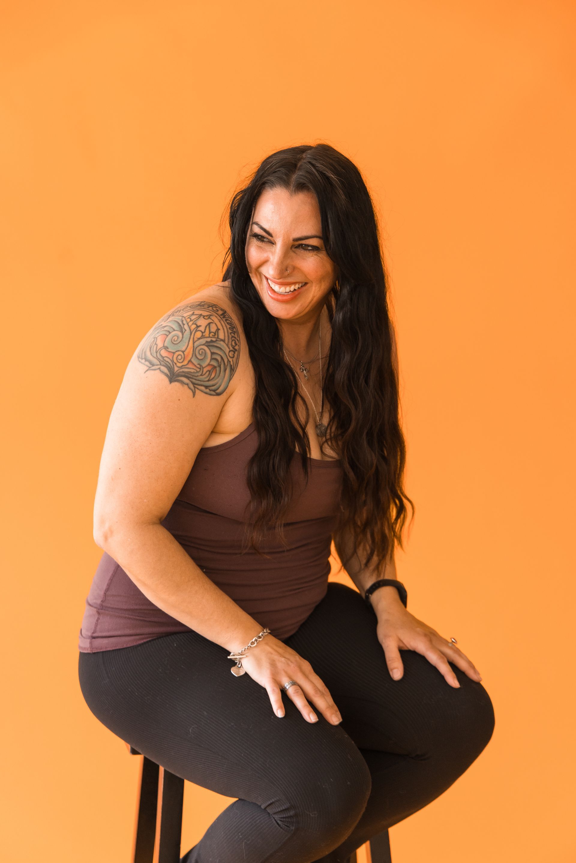 A woman is sitting on a stool with her legs crossed and smiling.