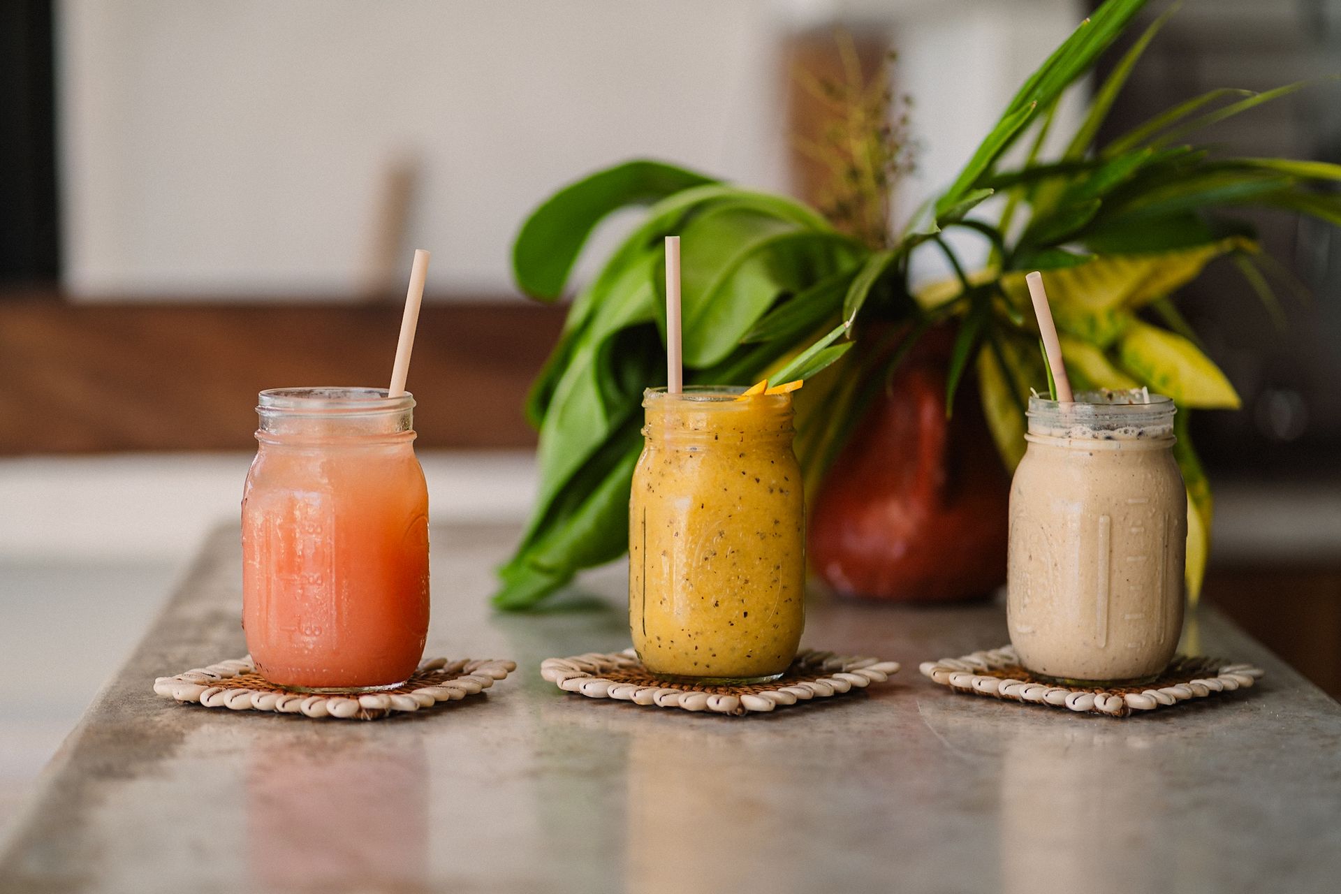 Three smoothies in mason jars with straws on a table.