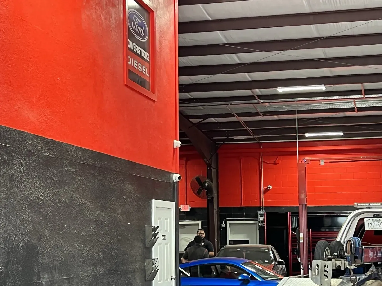 Interior of an auto repair shop with red and black walls. A blue car and mechanics are visible inside.