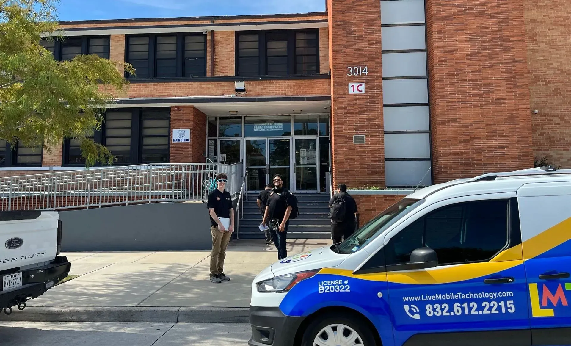 Exterior view of a brick building with people standing near the entrance and a service van parked in front.