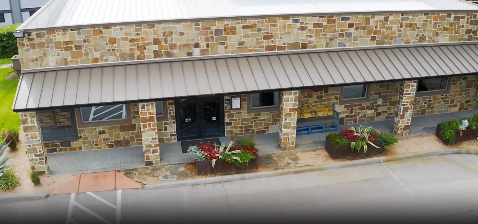 Building with stone facade, covered walkway, and flower beds in front.