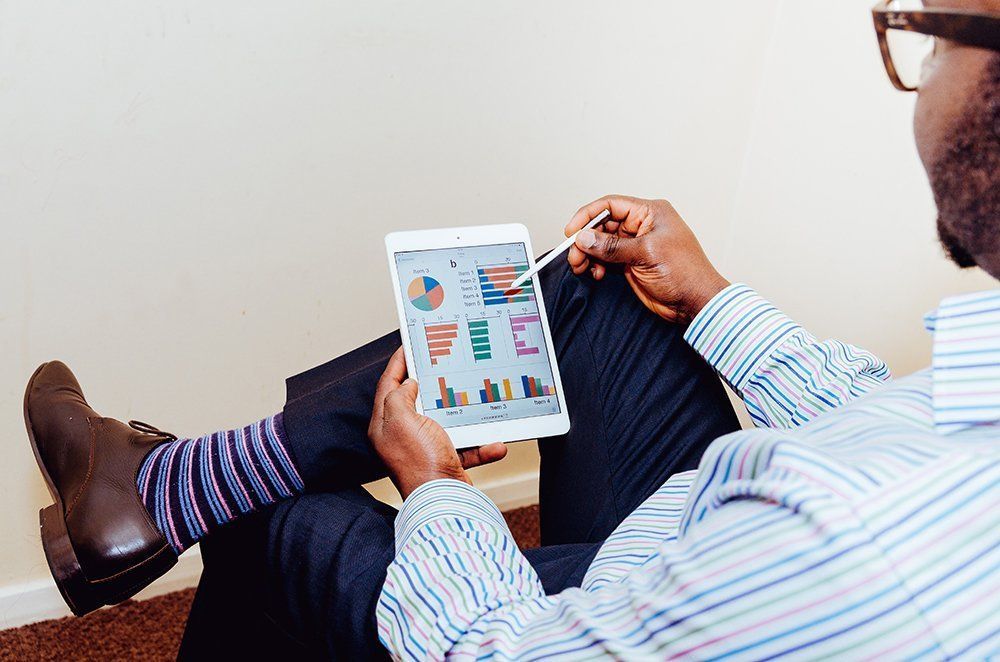 Man in striped shirt and blue pants looks at charts on a tablet, resting his feet up.