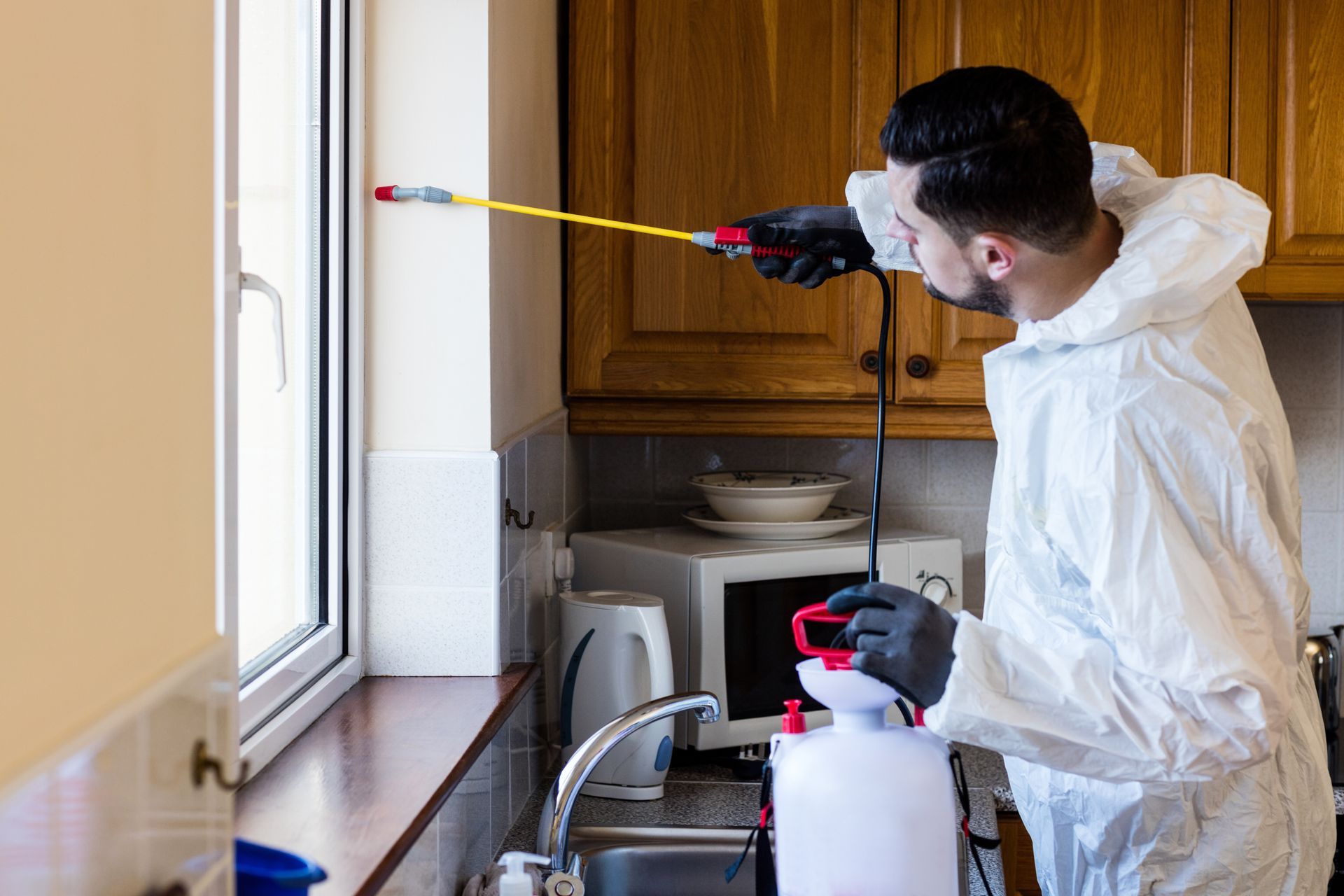 An exterminator is performing pest control services, spraying pesticides in the kitchen.