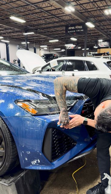 Person wrapping a blue sports car in a garage, with the hood open and foam covering the front