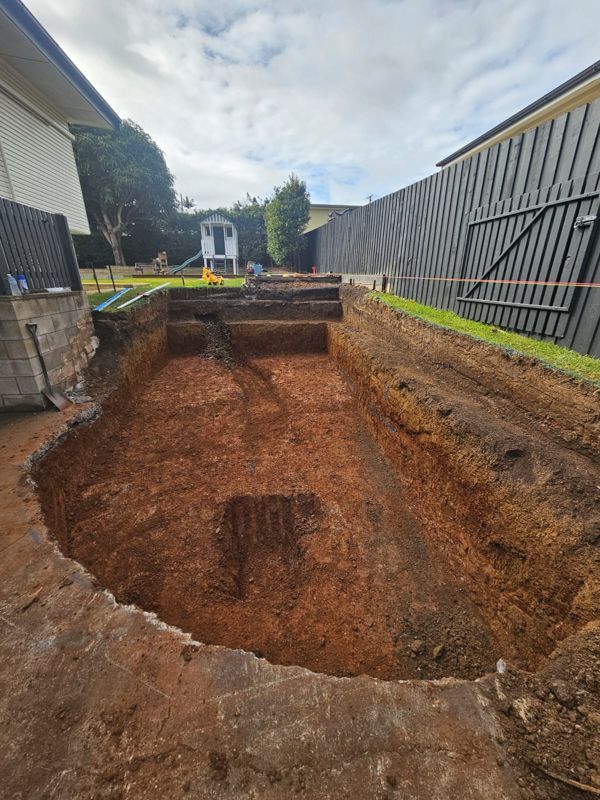 Excavation site with stepped levels, brown earth, residential backyard setting, overcast sky.