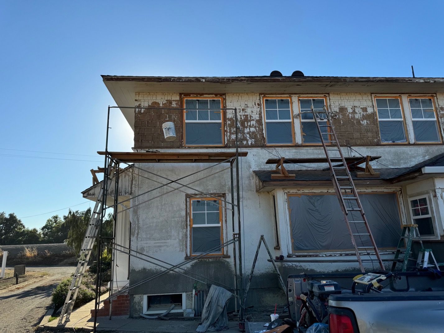 Damaged two-story house with scaffolding and ladders under a clear blue sky