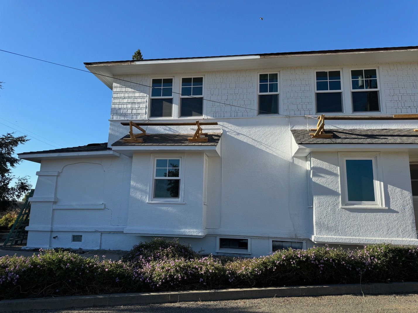 White two-story house exterior with balconies, blue sky, and hedges in front