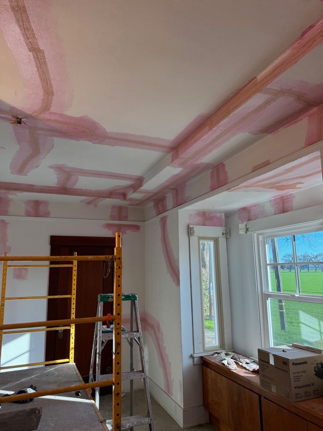 Renovating room with scaffolding, pink drywall seams, and a bright window over a countertop