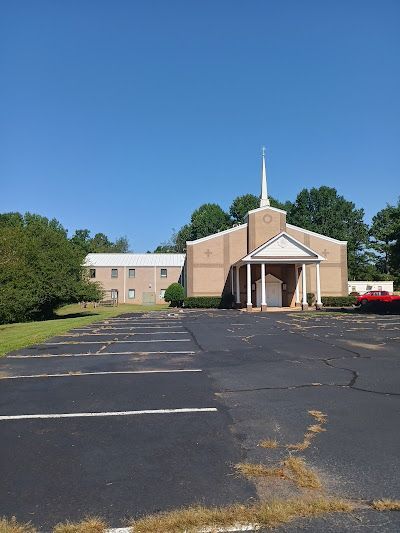 A church with a steeple is sitting in the middle of a parking lot.