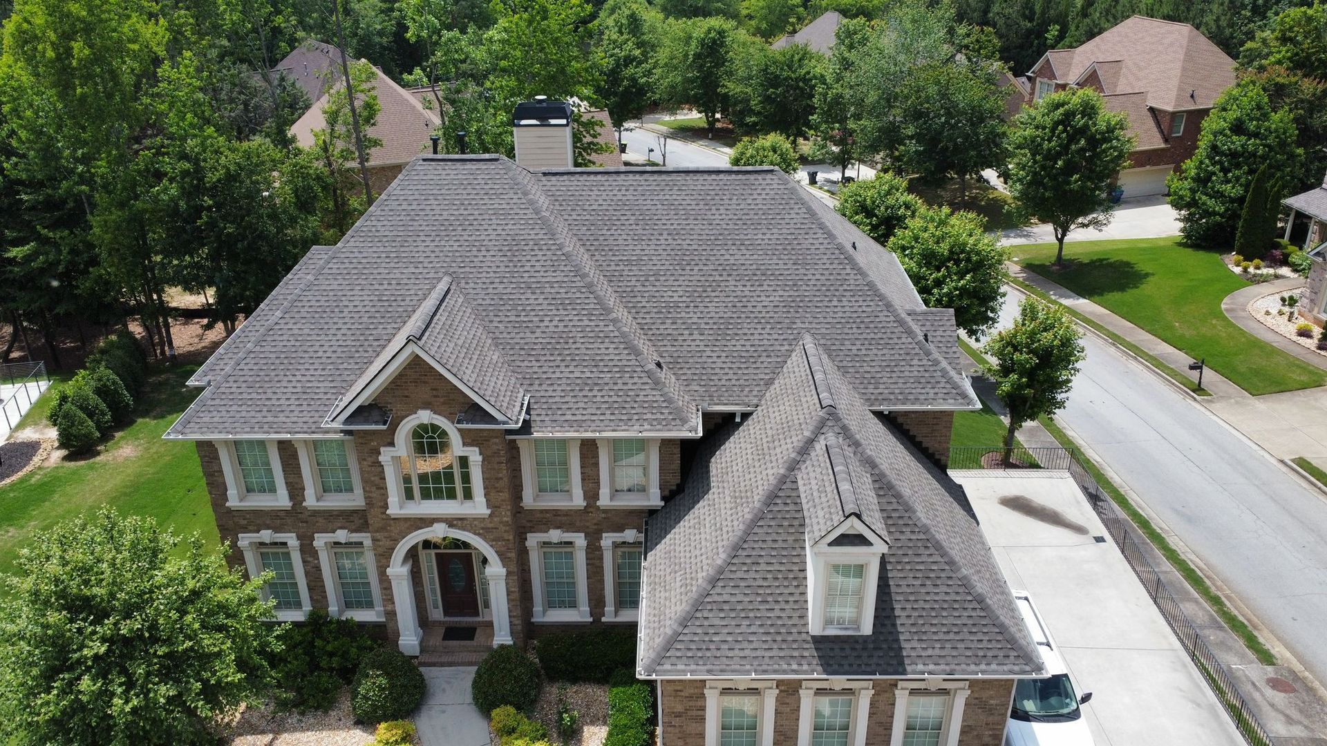 An aerial view of a large house in a residential area surrounded by trees.