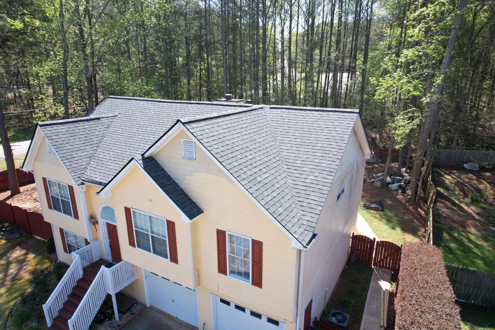 An aerial view of a house with a roof in the middle of a forest.