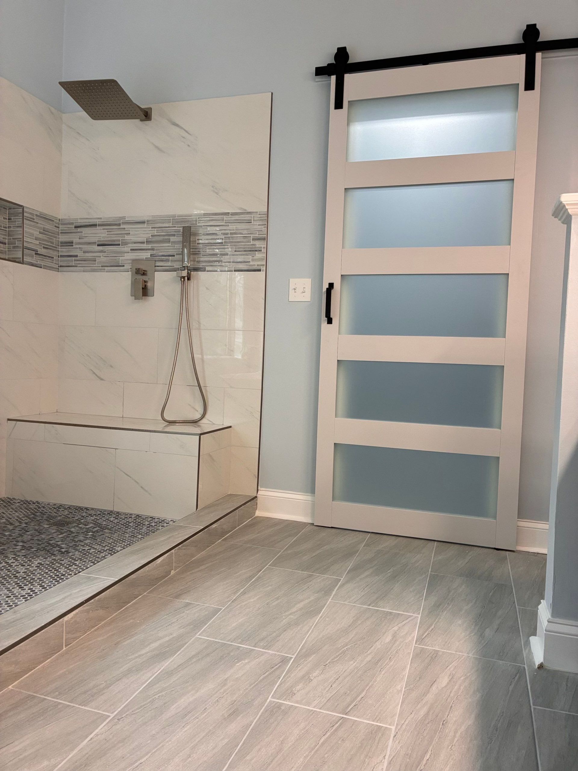 Modern bathroom: shower with stone floor and bench, sliding door with frosted glass. Light blue walls, gray tile.