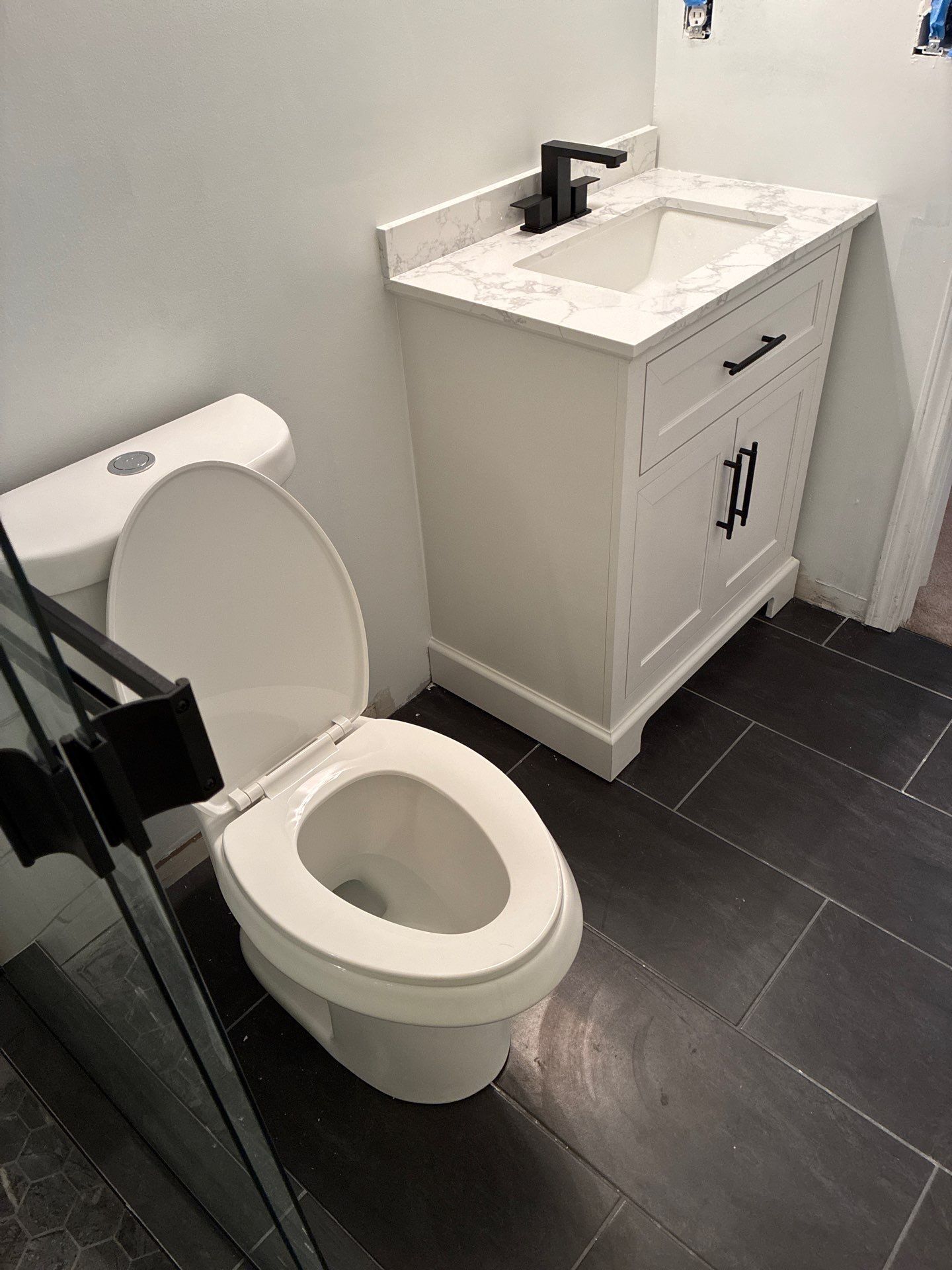 Bathroom with white toilet, vanity, and dark tiled floor. Black fixtures.